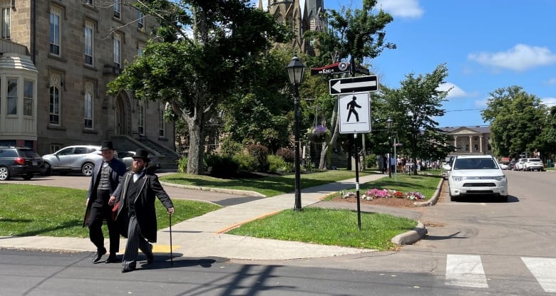 Two historical animators, known as Confederation Players, walk down Great George Street in Charlottetown with St. Dunstan's Cathedral and Province House in the background.