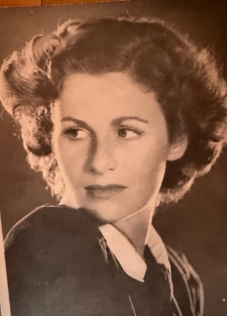 A woman with big beautiful eyes and feathered hair looks over her shoulder in an antique photograph