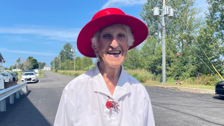 a woman stands outside wearing a bright red hat, white blouse and blue skirt