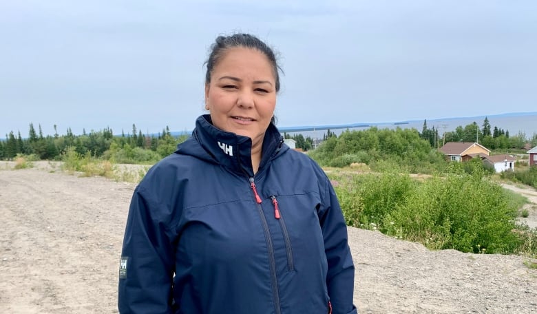 A woman stands on a gravel road, with a large lake behind her. 