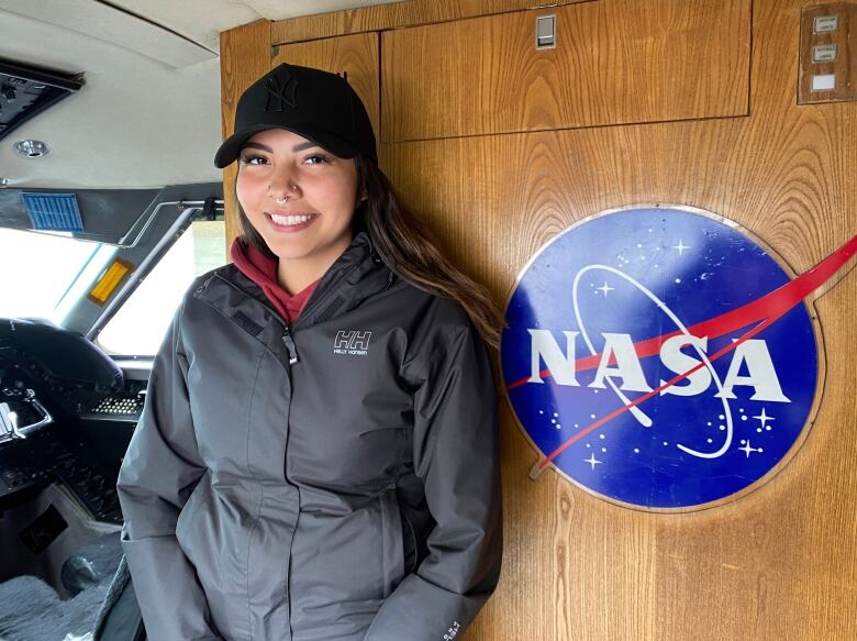 A woman stands in front of a sign that reads NASA.