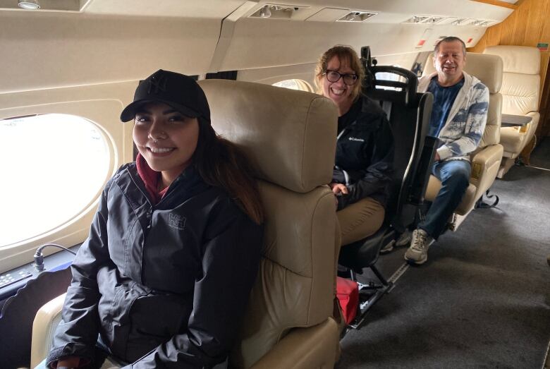 Three people sit on a plane. Looking real excited.