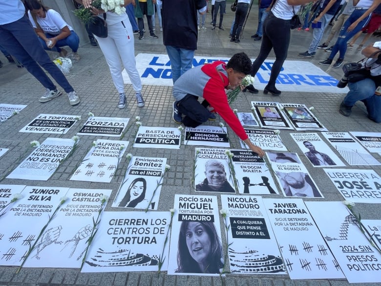 A young person holding flowers appears to be arranging posters on the ground. 