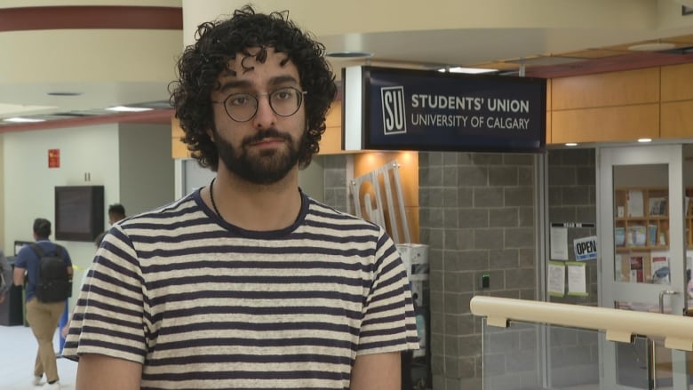 A close-up shot of a man in a striped T-shirt. He has curly hair and is wearing glasses.