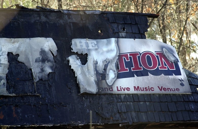 A charred shingled roof and ripped banner are shown in closeup.