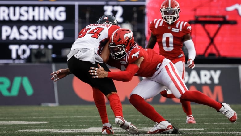 Three people are pictured on the field during a football game wearing red and black and white uniforms and helmets.