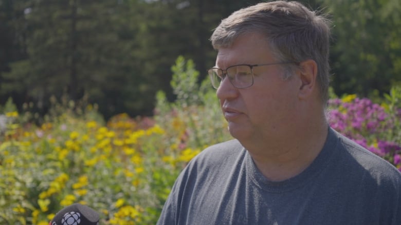 Steven Heard talks to a microphone held by Ben Ford of CBC, about the importance of growing flowers that are beneficial to pollinators native to the province.