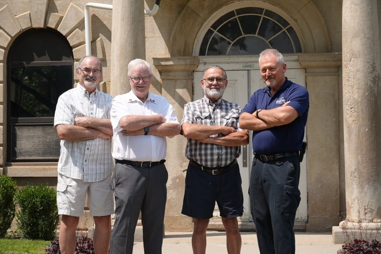 Four men standing outside an old building with their arms folded