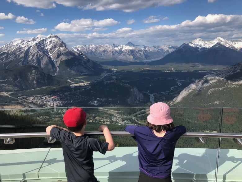 Two little children turned away from the camera. Large mountains in the background.