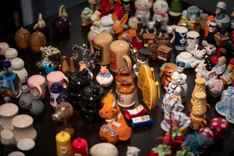 A range of salt and pepper shakers are pictured on a table. Some of them are shaped like animals and household objects.