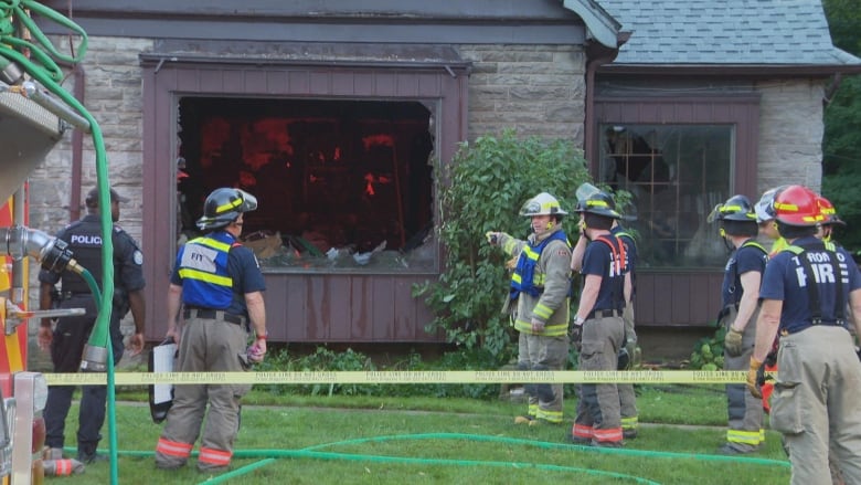 Firefighters stand outside of a home damaged in a fire.