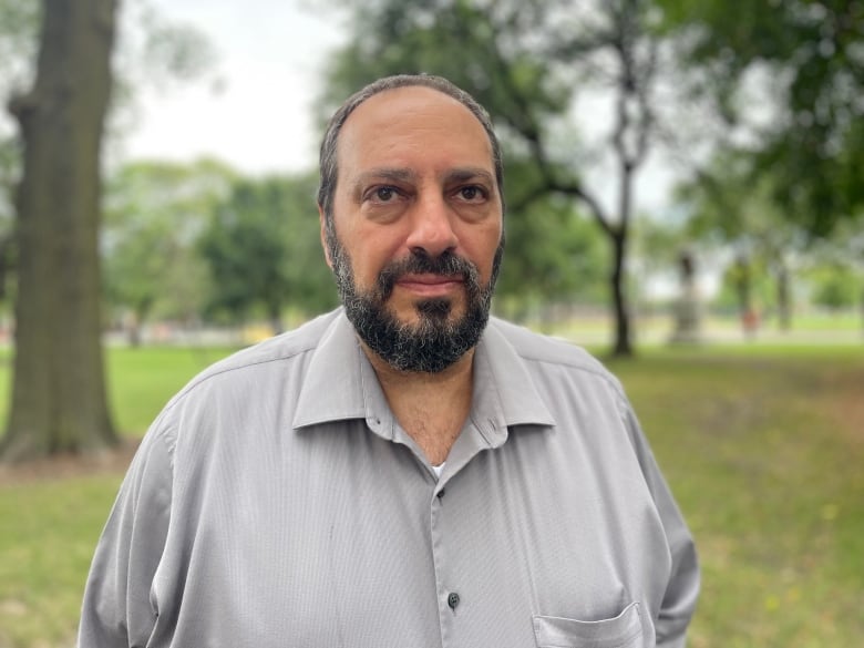 A man wearing a gray button down shirt stands outside.