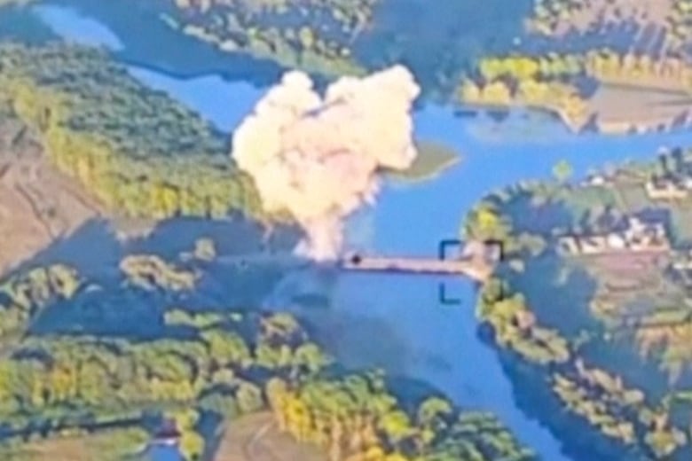 A large amount of smoke is shown from an aerial view on grainy video, over what appears to be a bridge over a body of a water.