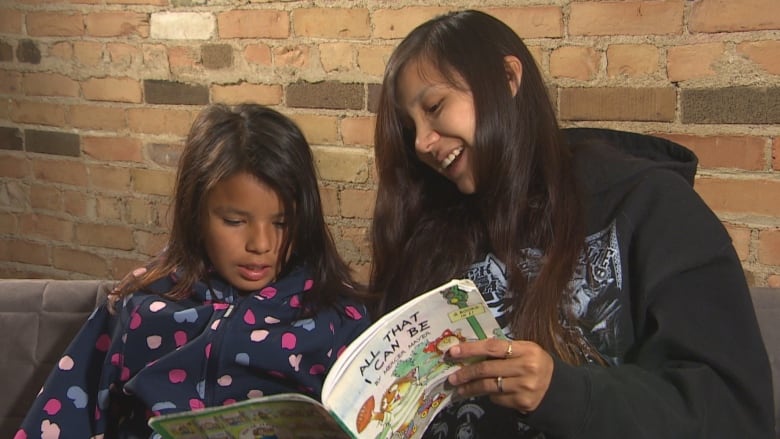 A woman and a young girl sit side-by-side and read a children's book.