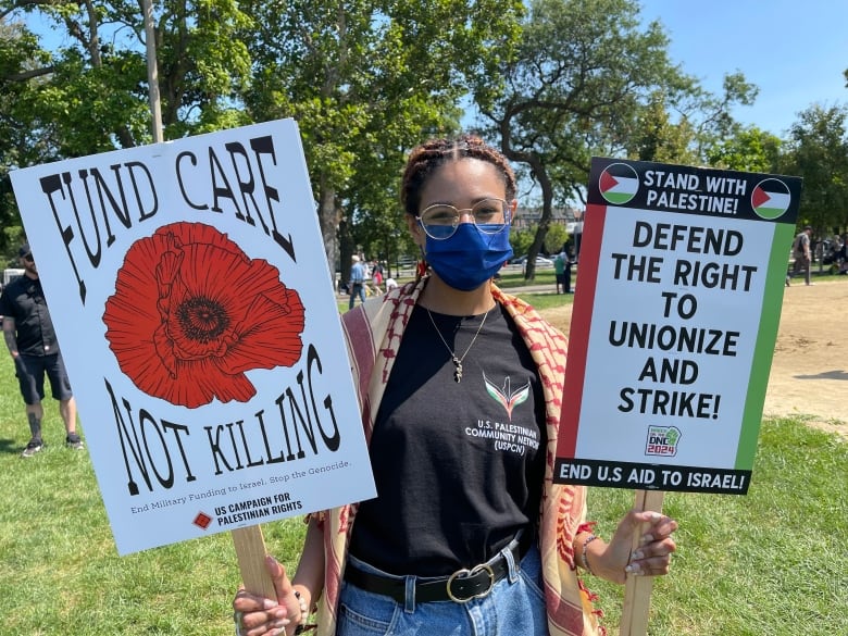 A woman wearing a mask holds two signs.