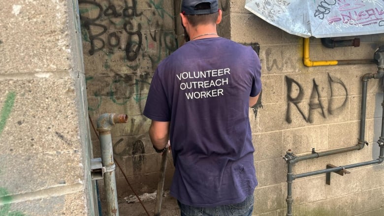 A man stands in front of a spray-painted door wearing a shirt that says 'volunteer outreach worker.'