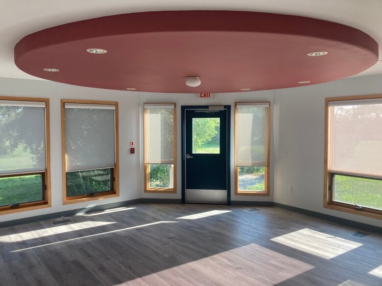 A room with five half-shaded windows and a door is empty. 