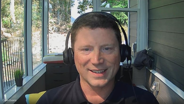 A man smiles while seated on an outdoor patio.