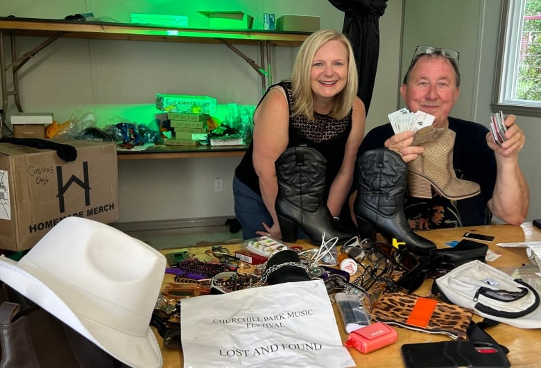 Man and women sitting behind a desk that includes a lot of stuff on it, including a single sparkly boot, a white cowboy hat, sunglasses and bags.