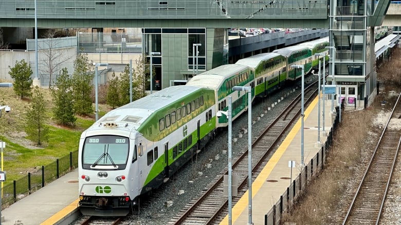 Seen from above, a train sits at a station under a bridge.