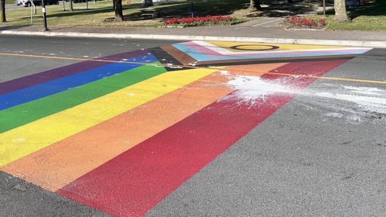 A painting of a pride flag along a crosswalk with some white paint splattered over it.