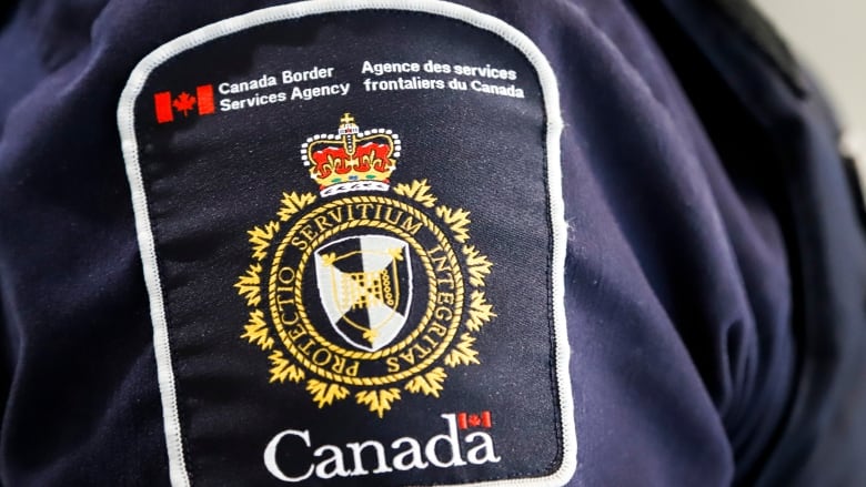 A blue uniform with a shoulder patch has a crown on top and the word Canada on the bottom separated by a circular logo with the Latin inscription, Protectio Servitium Integritas.