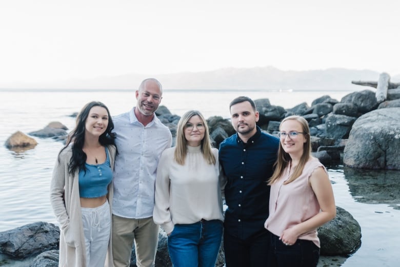 A family of five pose by ocean waters, with giant boulders behind them.