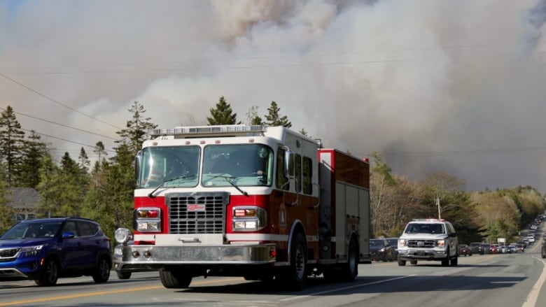 A firetruck is seen travelling away from a massive plume of smoke