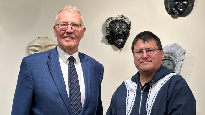 Two men stand side by side in a room.