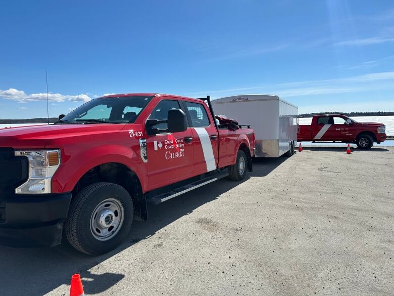 Two red trucks on a boat launch.