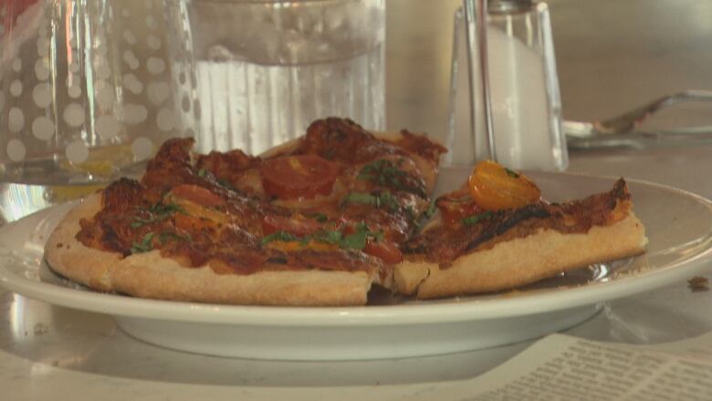 A pizza is shown on a white plate at a restaurant. 