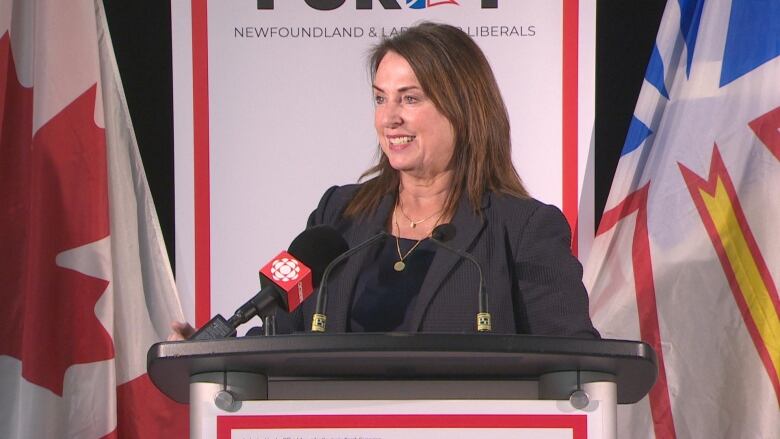 Woman in dark suit smiling behind a podium.