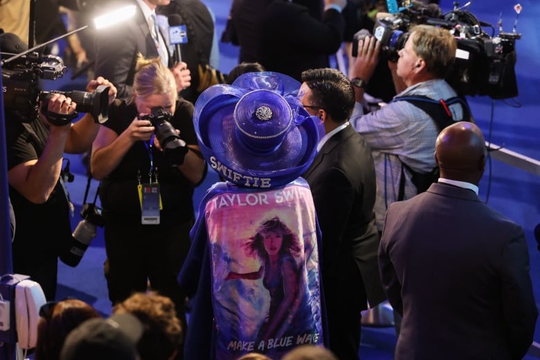 A person in Taylor Swift attire is photographed at a convention