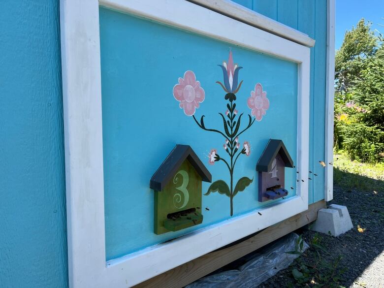 A side of a blue painted wall with bees flying into an entrance.