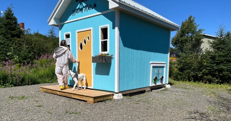 Person in white protestive gear walking towards a blue-painted hut.