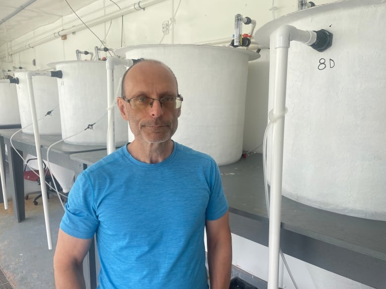 A man in a blue Tshirt stands in front of large white plastic tubs 