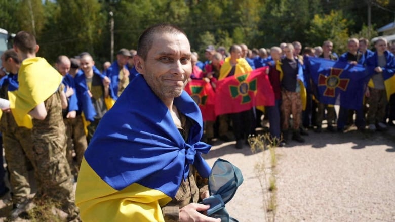 A man wrapped in a flag smiles outside.