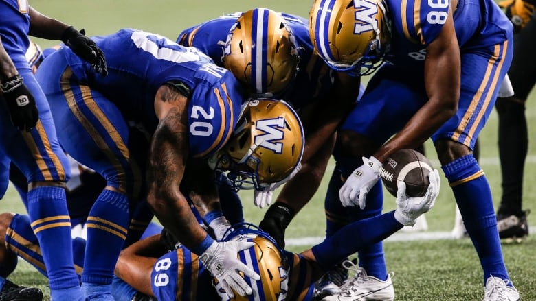 A group of football players embrace one of their own, who is on the ground.