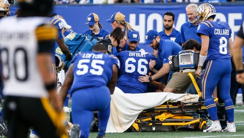 A group of people surround a football player who sits on a stretcher.