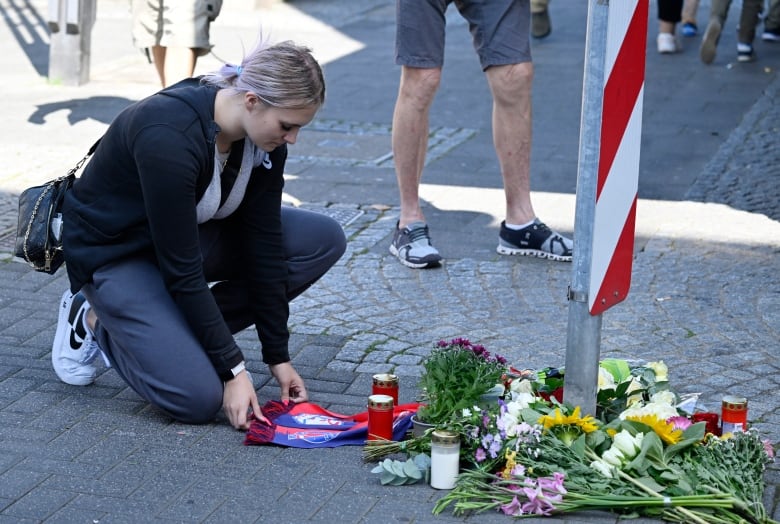 A person kneels to place a scarf at a makeshift memorial of flowers and candles.