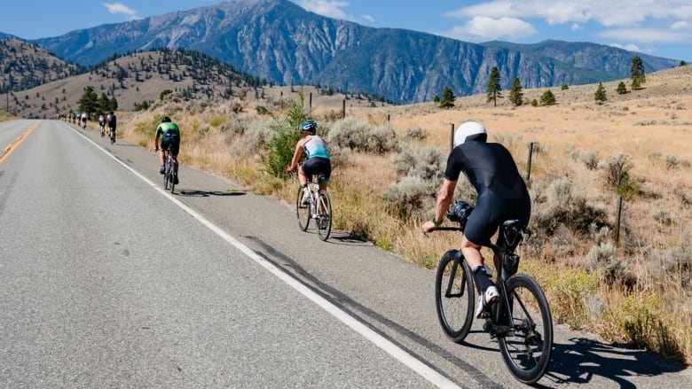 Bunch of bikers riding through a highway with hills and mountain in the background.