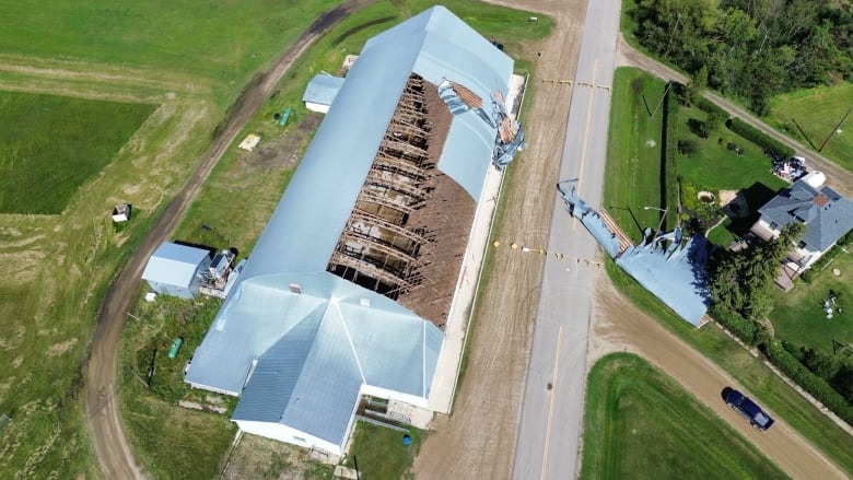 A bird's eye view of an arena with part of its roof ripped off and laying on a nearby road.