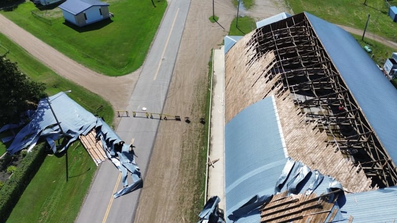 A building has a part of its roof missing, some of the debris lays on the ground next to the building.