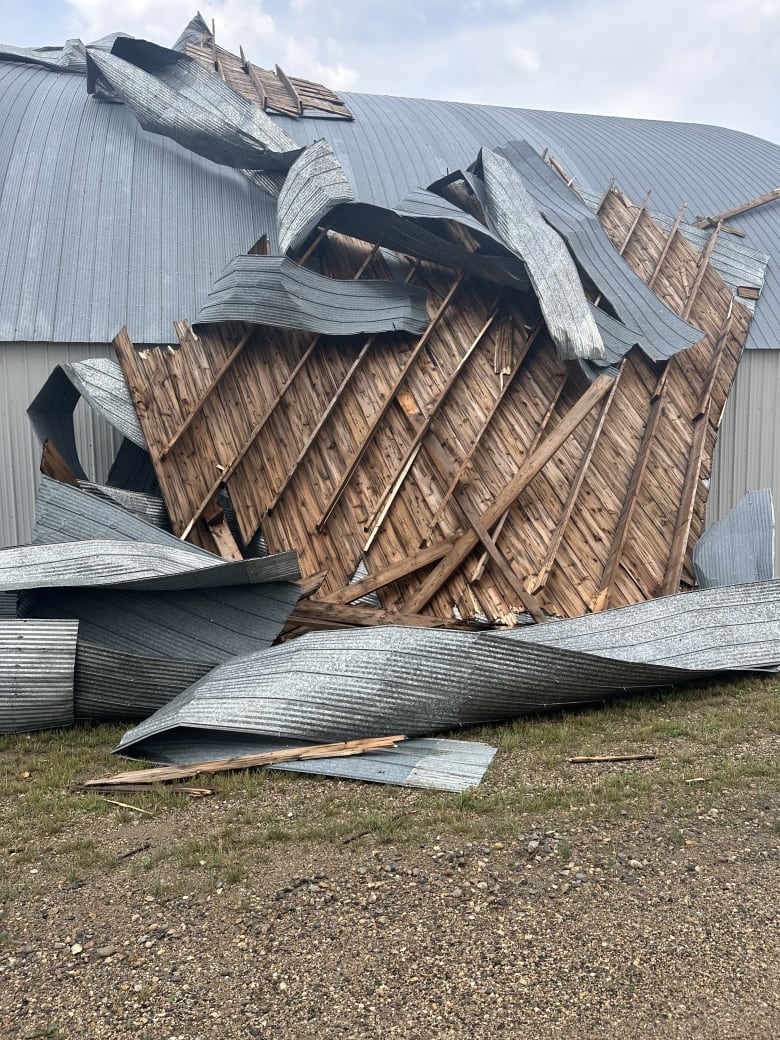 Portion of a metal and wooden roof stands on the ground, besides a building.