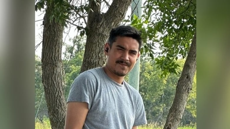 A man with short, black hair, wearing a grey t-shirt looks forward at the camera.