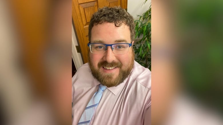 A person wearing a pink dress shirt and light blue tie takes a selfie.