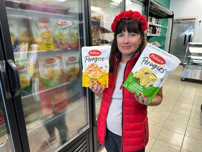 A woman in a red vest and red headband holds two bags of perogies. 