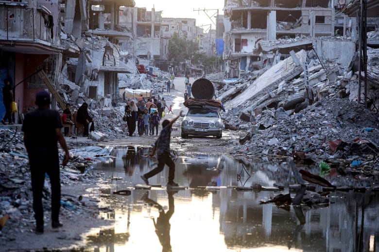 People walk down a street lined with mud, water, trash and rubble