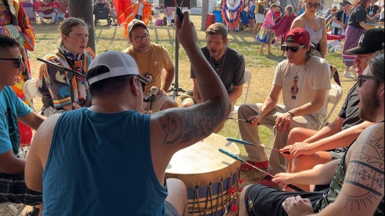 men gathered around a powwow drum seen drumming.