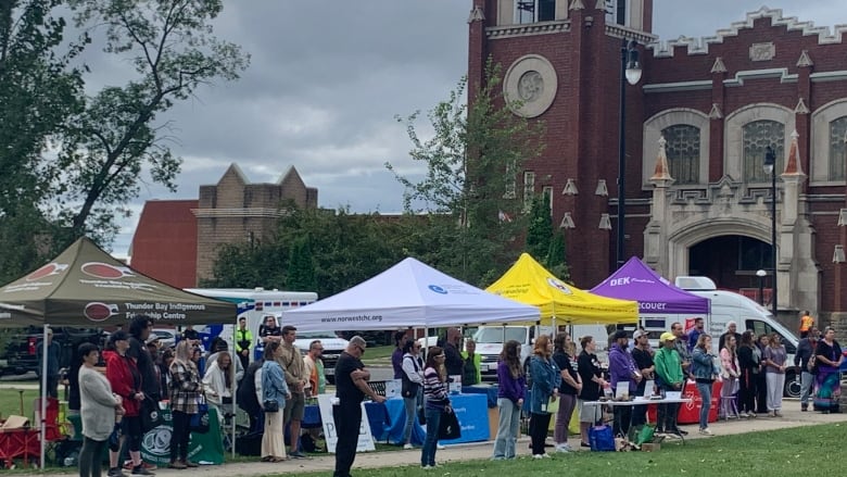 A group of people stand in a park near information booths.